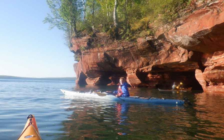 a student paddles a kayak beside a tall red cliff
